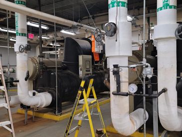 Industrial pipes and machinery in a facility with a yellow ladder.
