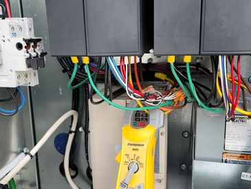 Electrical panel with colorful wires and a yellow Fluke device connected.