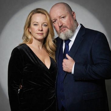 A couple posing together in formal attire against a plain backdrop.