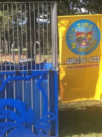 A dunk tank with a bright yellow banner in a park setting.