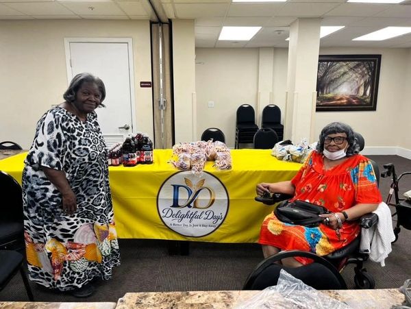 Two elderly women by a table with 'Delightful Days' banner.