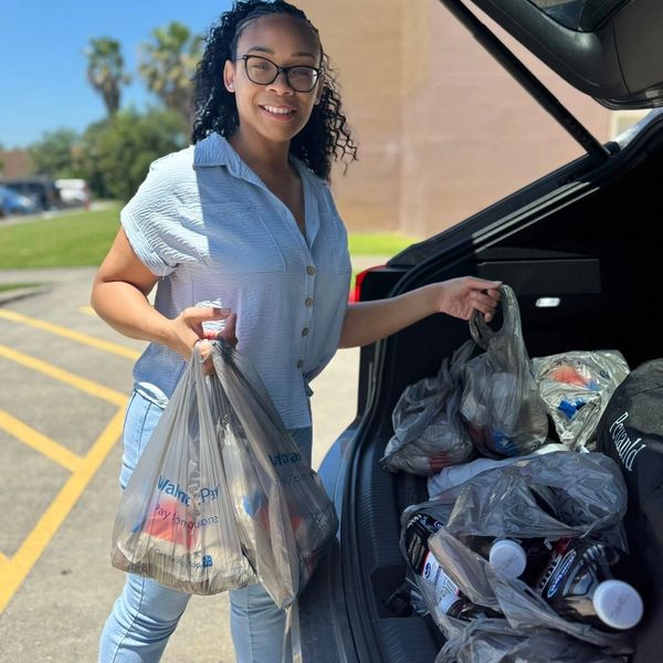 Smiling woman unloading groceries into car trunk.