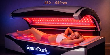 Woman relaxing in a red light therapy bed labeled SpaceTouch.