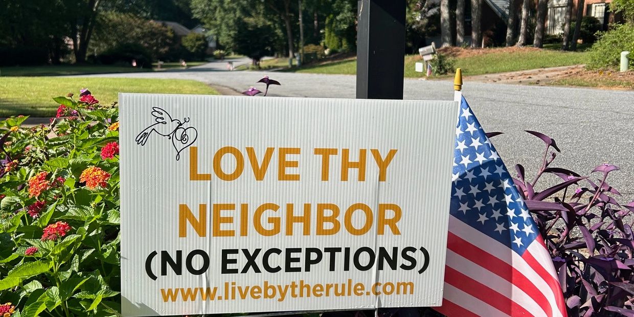 Sign reading 'Love Thy Neighbor (No Exceptions)' with an American flag.