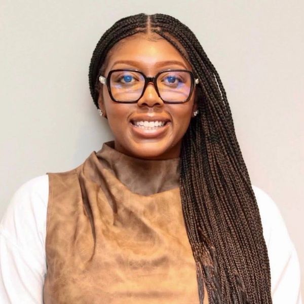 Smiling woman with long braided hair and glasses wearing a brown top.