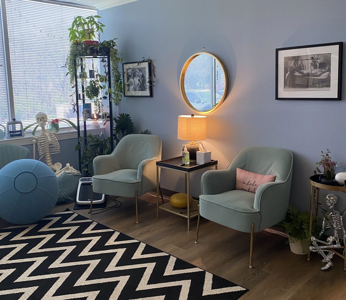Cozy room with green chairs, plants, skeletons, and framed pictures on blue walls.