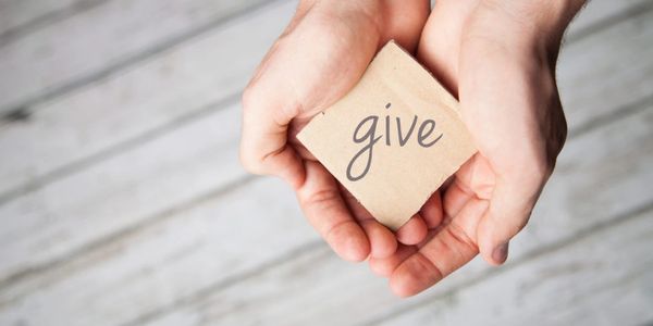 Hands holding a paper cube with the word 'give'.