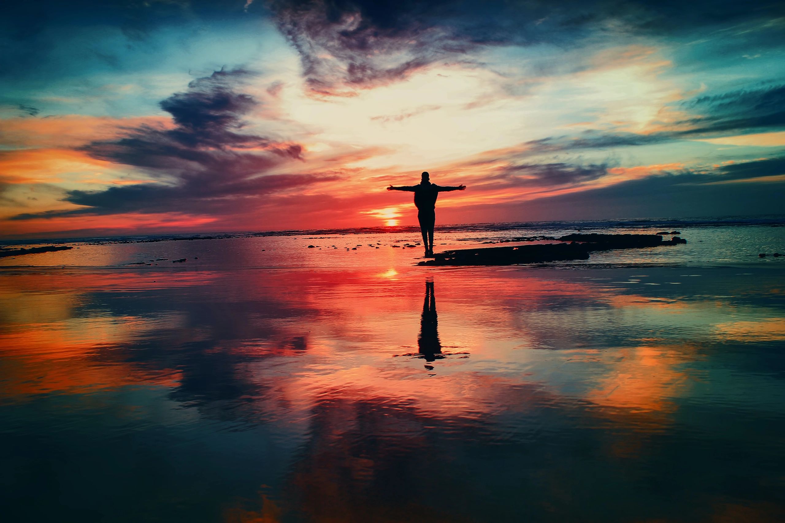 Person standing in shallow water near the ocean at sunset