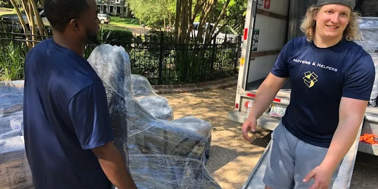 Two movers handling wrapped furniture near a moving truck on a sunny day.
