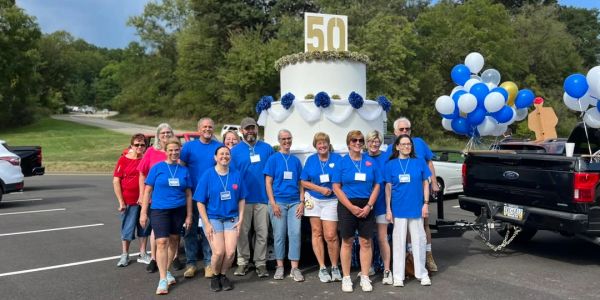 Group photo celebrating a 50th anniversary with a large cake and balloons.