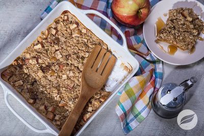 Baked apple oat crumble in a white dish with a wooden spatula.