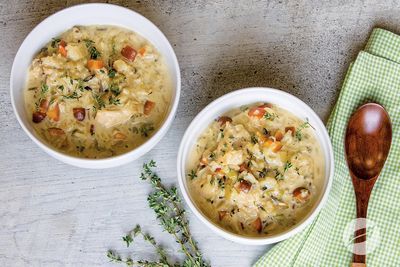 Two bowls of creamy chicken and wild rice soup with herbs on a rustic surface.