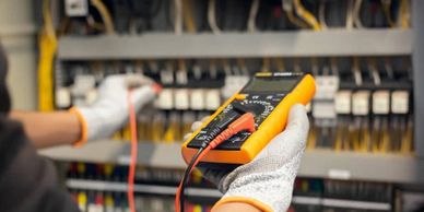Electrician using a multimeter to test wiring in a control panel.