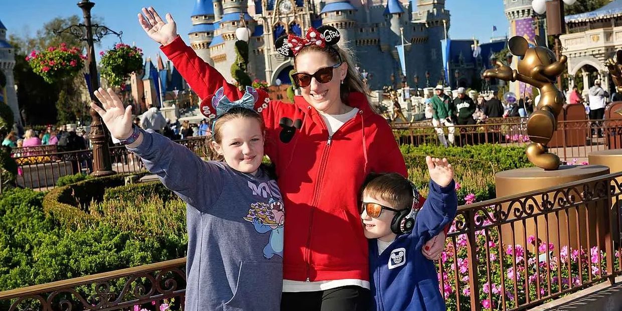 Family posing happily at a theme park in front of a castle.