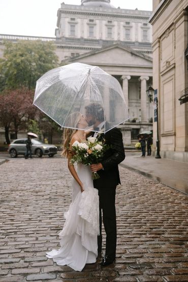 Couple s'embrassant sous la pluie dans le Vieux-Montréal, le marié tient le bouquet de la mariée