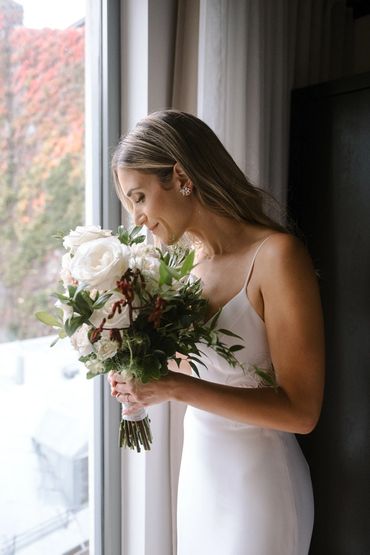 Future mariée avec sa robe admirant son bouquet de fleurs devant la fenêtre de sa chambre à Montreal