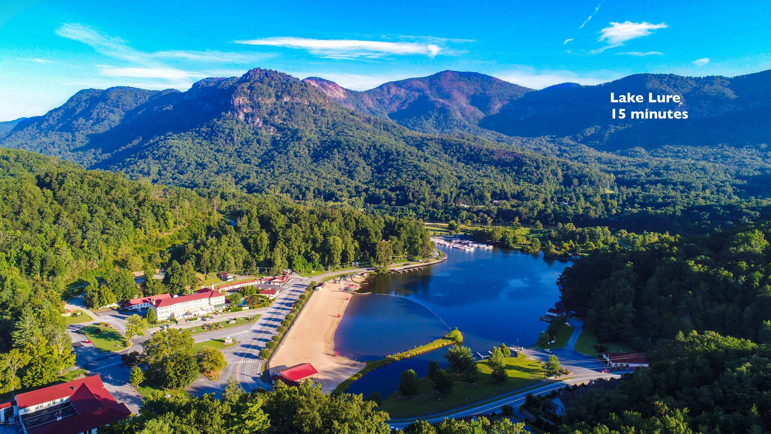 A scenic lake with a beach surrounded by mountains and lush greenery.