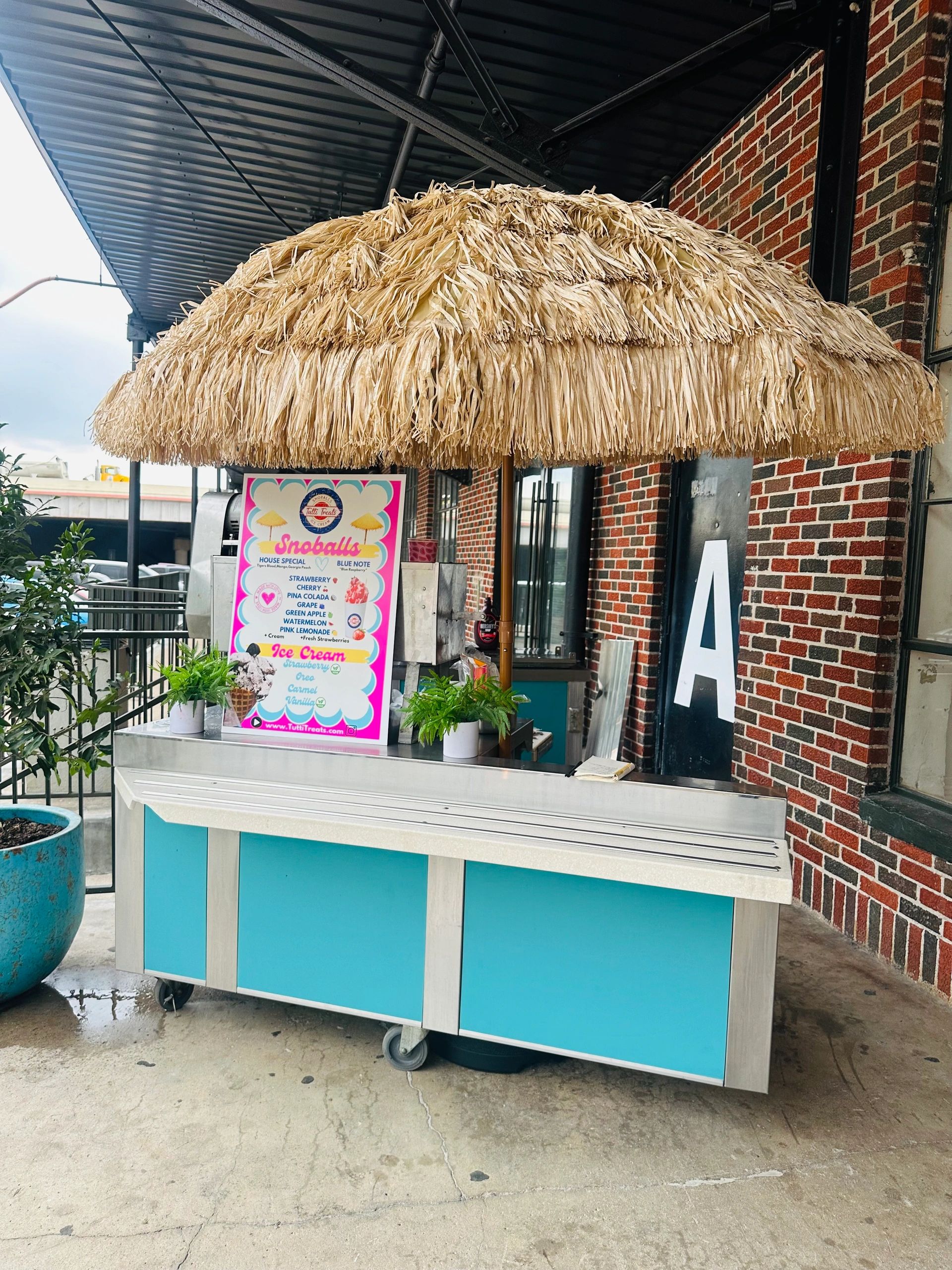Outdoor snack cart with a thatched umbrella and colorful menu.