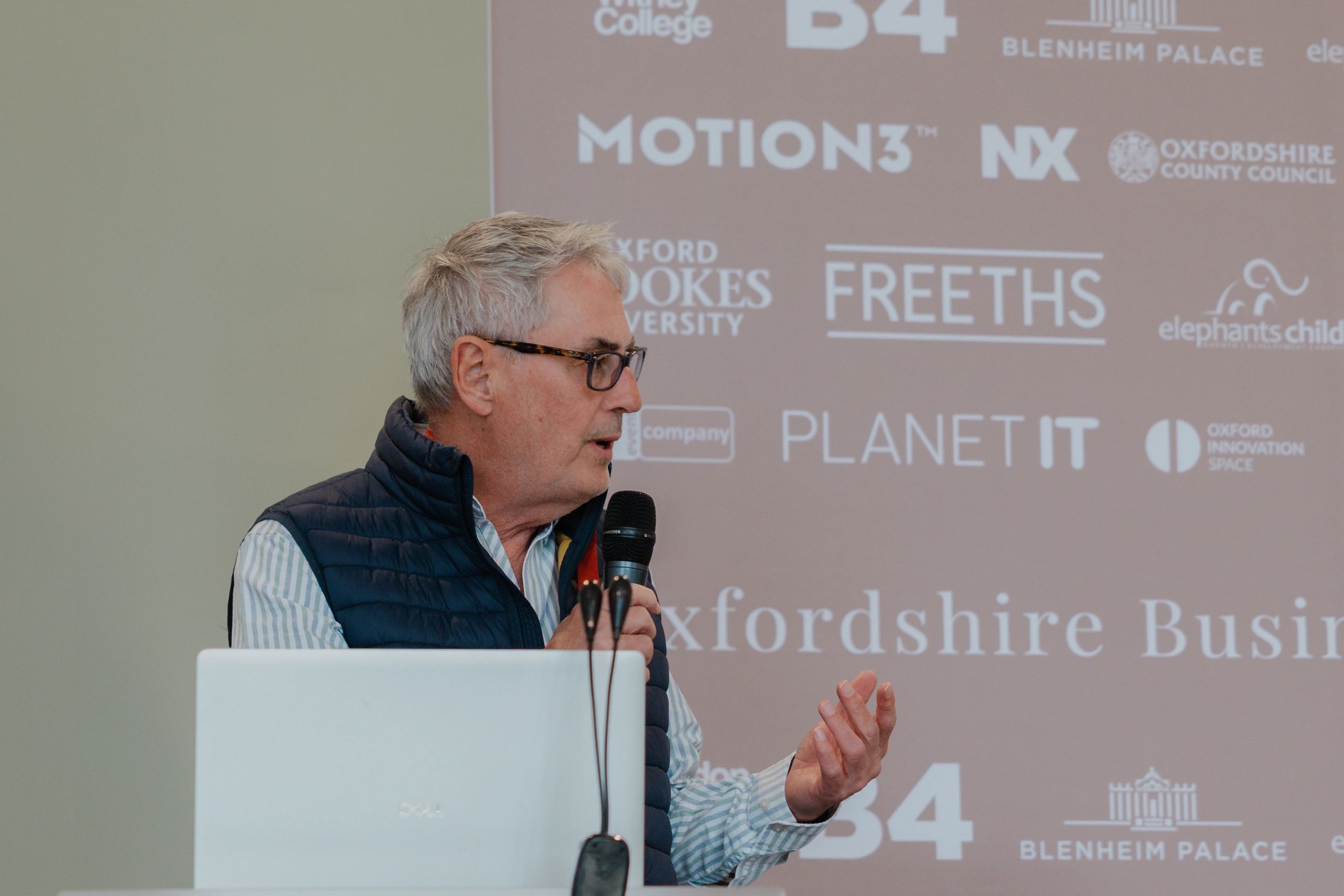 Man speaking at a conference with logos in the background.