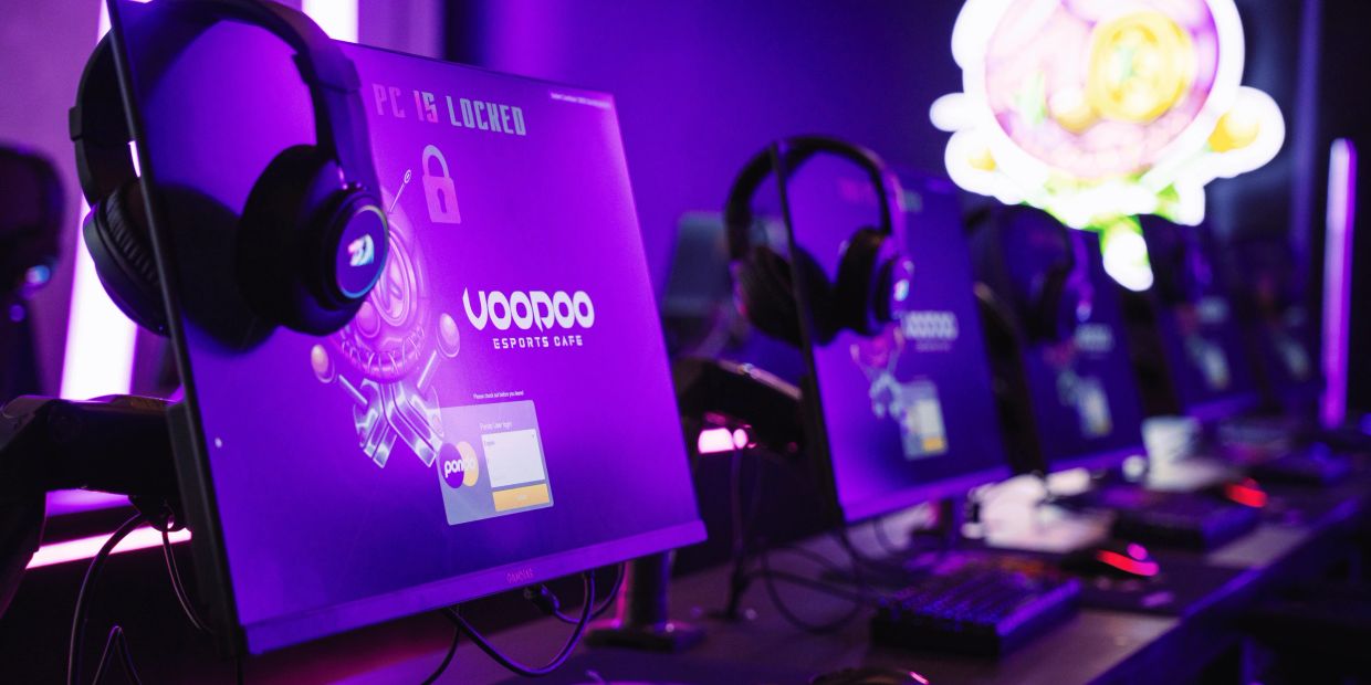 Row of gaming monitors with headphones in a purple-lit esports cafe.