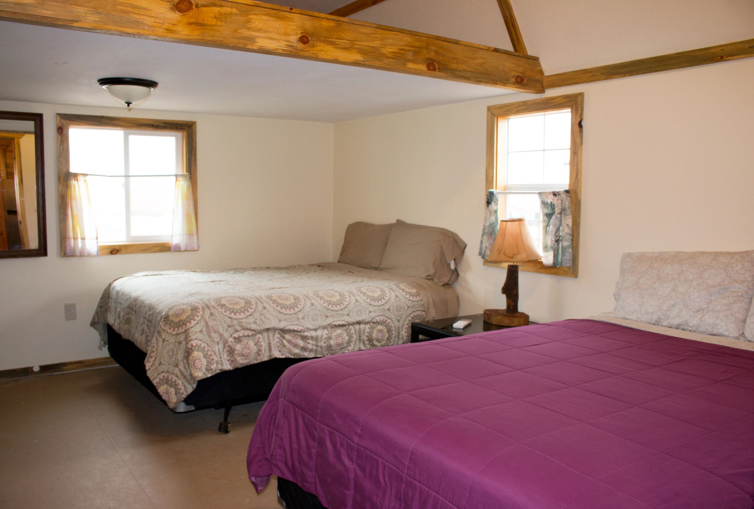 Cozy bedroom with two beds, wooden accents, and natural light from windows.