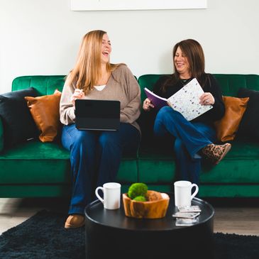 Two women sitting and laughing on a green couch.