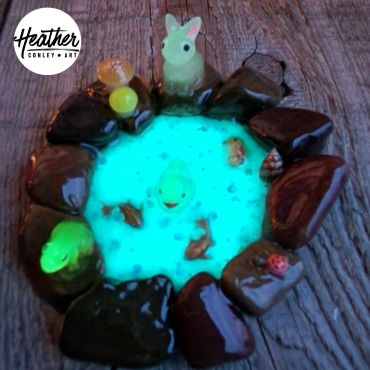 Miniature glowing pond with animals and rocks.