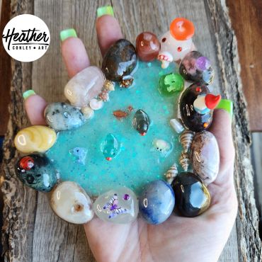 Hand holding colorful polished stones around a blue resin pool.