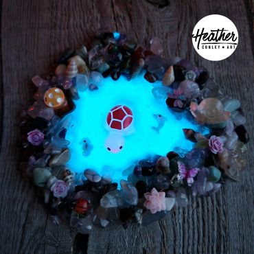 Glowing blue resin turtle art surrounded by small seashells and ornaments.