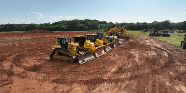 A lineup of yellow bulldozers and excavators on a dirt field under a clear sky. Excavation services.