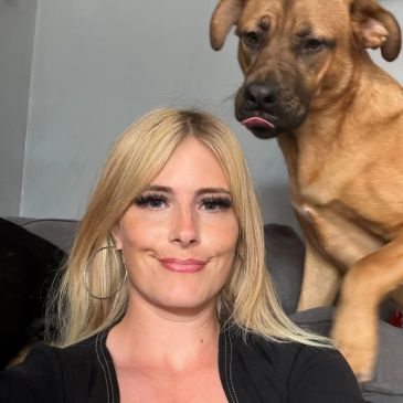 Woman making a funny face with a dog licking its lips behind her.