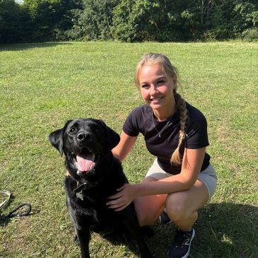 Young woman smiling with her black dog outdoors on a sunny day.