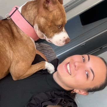 A woman smiling with a brown dog wearing a pink collar.