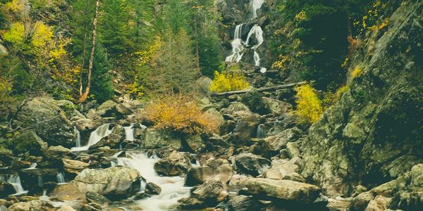 A serene waterfall cascades over rocks surrounded by autumn trees.