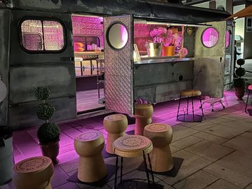 Nighttime scene of a vintage food truck with champagne cork stools and purple lighting.