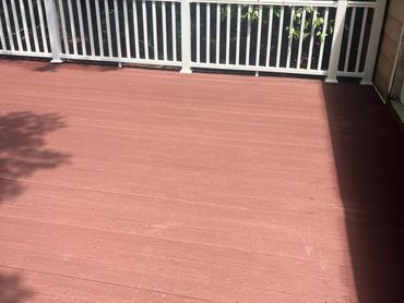 Empty red wooden deck with white railing under sunlight.