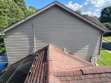 View of a rooftop with shingles and a house wall under a clear blue sky.