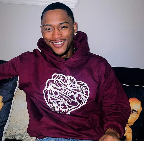 Man smiling wearing a maroon hoodie with a domestic violence awareness design.