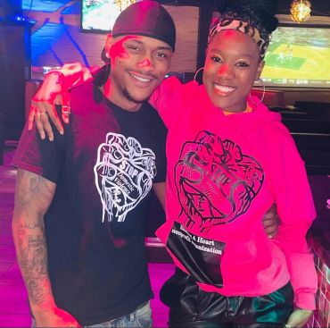Two smiling friends wearing matching shirts with a fist design in a lively bar setting.