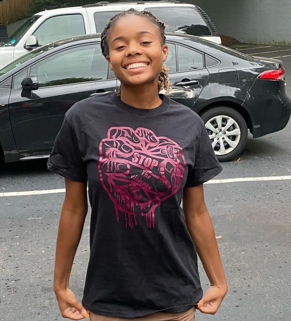 A smiling young woman wearing a black t-shirt with a stop violence graphic.
