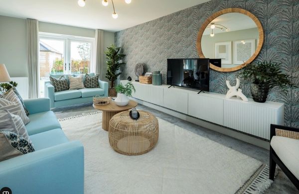 Modern new build living room with light blue sofas, patterned feature wall, and round mirror above m