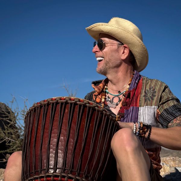 Man wearing a cowboy hat playing a large drum outdoors.