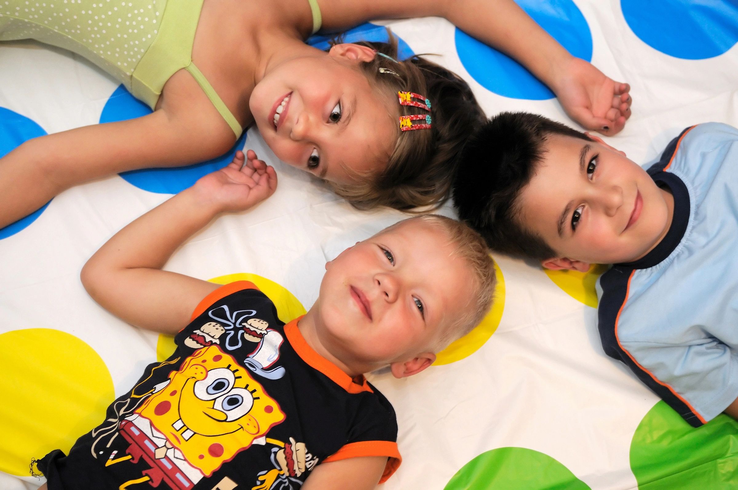 Three kids lying on a colorful polka dot mat, smiling.