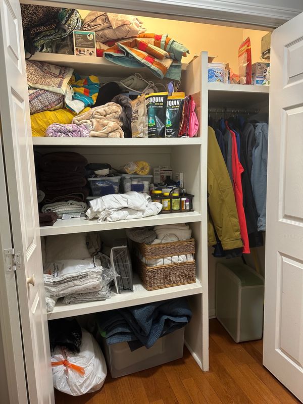 Organized closet with folded blankets, clothes, and jackets hanging.