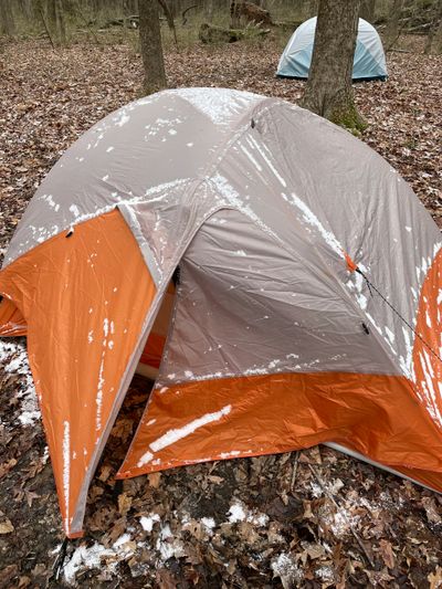 Orange and gray tent with snow on it in a wooded area.