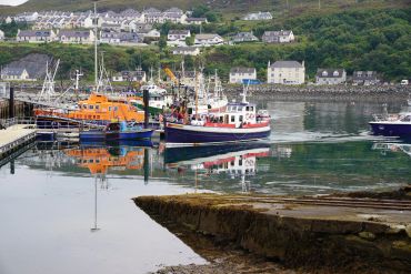 Colorful boats docked in a calm harbor with houses on a hillside.