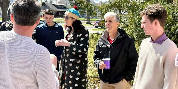 A group of people chatting outdoors on a sunny day, holding drinks.