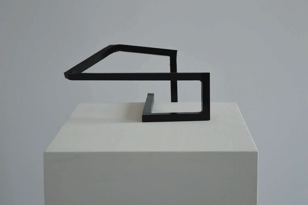 Back view of a dark green shape of square steel bars on top & in the middle of a white plinth.