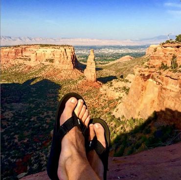 A person wearing black sandals with a canyon as a background