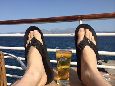 A person wearing black flip flops on a boat with a drink